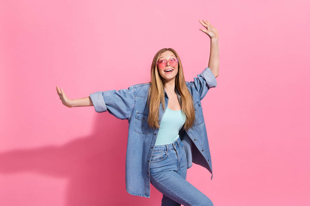 Foto portret van aantrekkelijke jonge tiener vrouw verhogen handen dans hebben plezier dragen trendy jeans kleding geïsoleerd op roze kleur achtergrond. - Foto, afbeelding