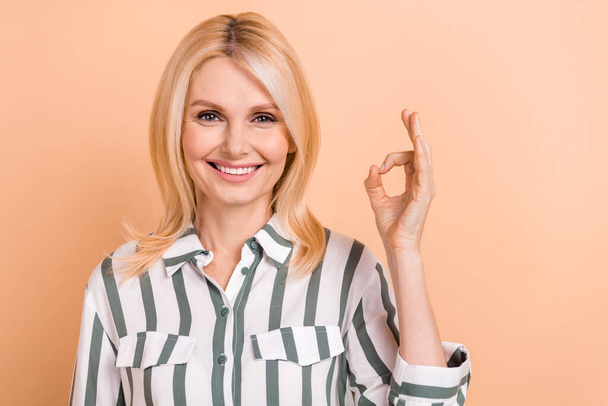 Photo of cheerful confident lady wear striped shirt smiling showing okey gesture isolated beige color background. - Foto, Imagen