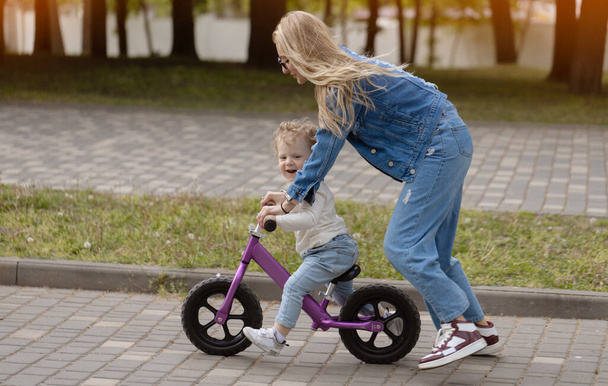 Young mother teaches her little son how to ride a balance bike in the park - Foto, Imagem
