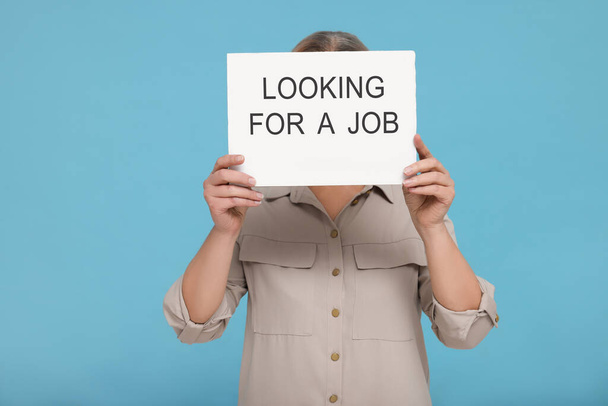 Unemployed senior woman holding cardboard sign with phrase Looking For A Job on turquoise background - Photo, image