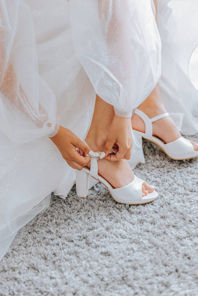 Bride putting on her white shoes. Beautiful bride getting ready for wedding. A woman trying on shoes. - Фото, зображення