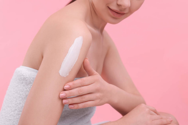 Woman with smear of body cream on her shoulder against pink background, closeup - Fotó, kép