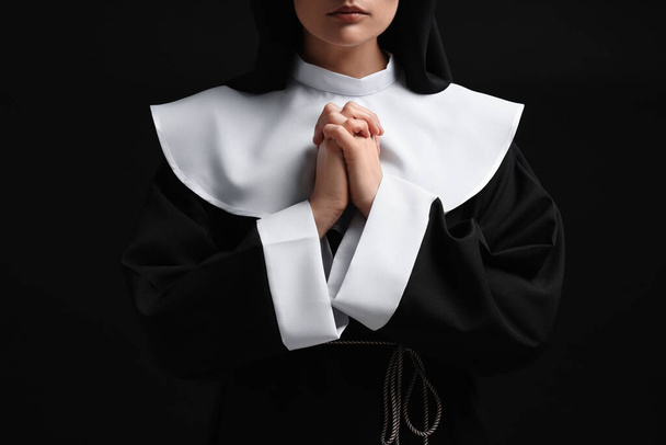 Nun with clasped hands praying to God on black background, closeup - Фото, зображення