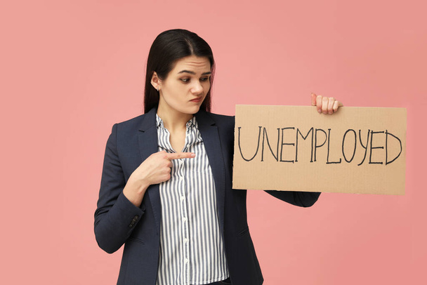 Unhappy woman holding sign with word Unemployed on pink background - Foto, imagen