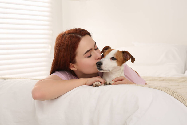 Woman kissing cute Jack Russell Terrier dog on bed at home - Fotografie, Obrázek