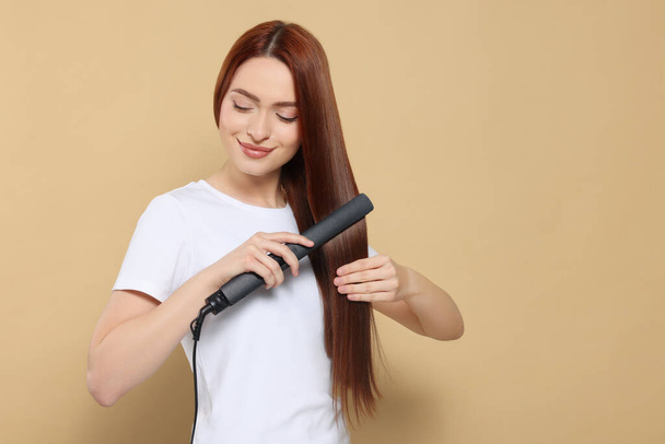 Beautiful woman using hair iron on beige background, space for text - Photo, Image