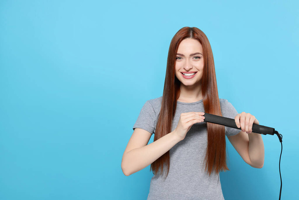 Beautiful woman using hair iron on light blue background, space for text - Foto, Imagem