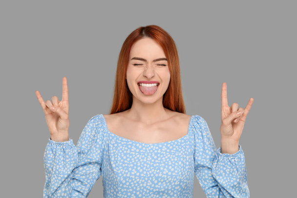 Happy woman showing her tongue and rock gesture on gray background - Photo, image