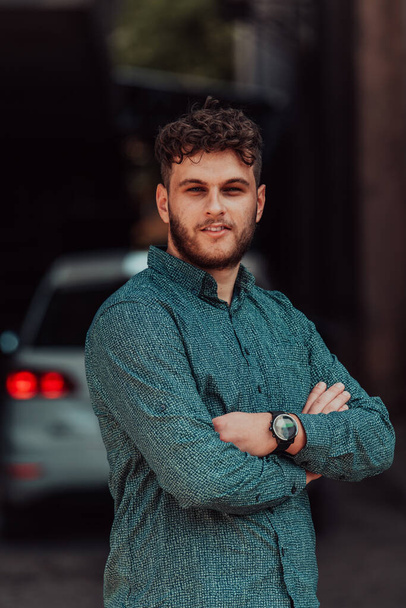 A successful young businessman in a shirt, with crossed arms, poses outdoors, confident expression on his face - Fotoğraf, Görsel