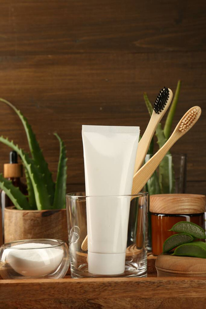 Aloe vera toothpaste in blank tube, brushes, green leaves and care products on wooden tray, space for text - Fotoğraf, Görsel