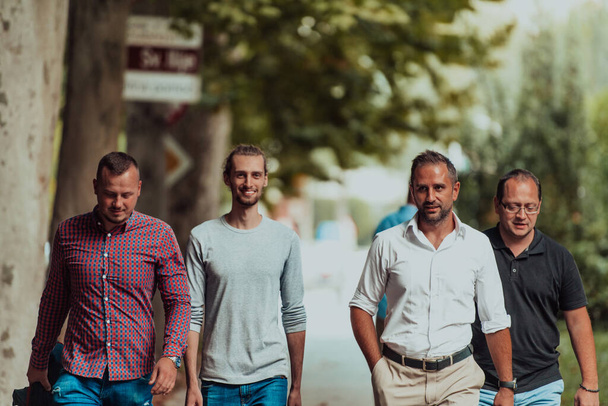 After a productive day at work, a group of diverse colleagues enjoy a leisurely stroll through a modern and natural urban setting. - Фото, изображение