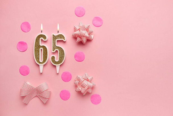 Número 65 sobre fondo rosa pastel con decoración festiva. Feliz cumpleaños velas. El concepto de celebrar un cumpleaños, aniversario, fecha importante, vacaciones. Copiar espacio. banner - Foto, imagen