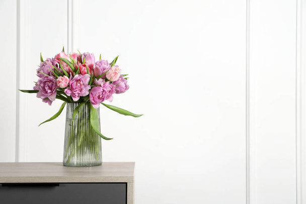 Beautiful bouquet of colorful tulip flowers in vase on wooden bedside table - Fotó, kép