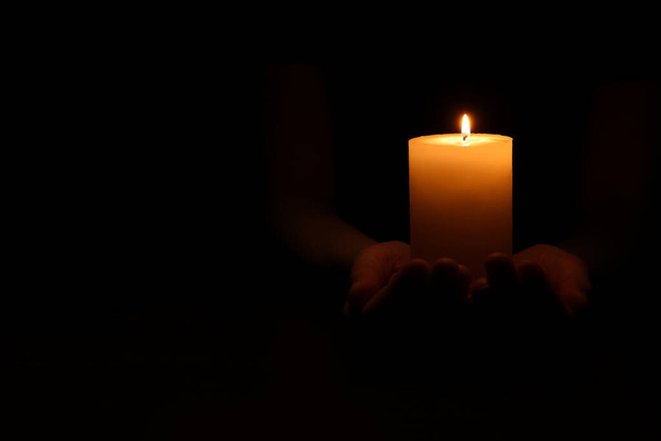 Woman holding burning candle in hands on black background, closeup. Space for text - Valokuva, kuva