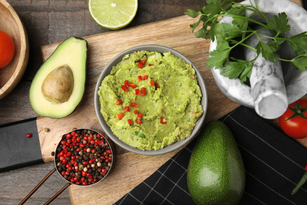 Bowl of delicious guacamole and ingredients on wooden table, flat lay - Fotoğraf, Görsel