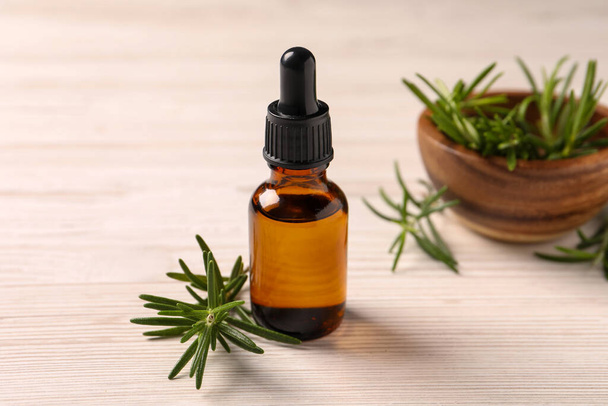 Bottle with essential oil and fresh rosemary on white wooden table - Foto, Imagen