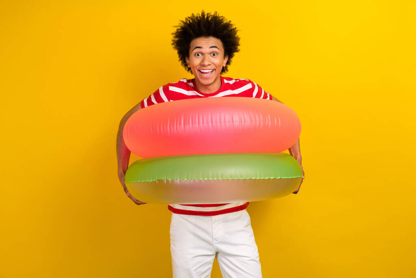 Photo of cheerful excited man dressed red t-shirt holding two inflatable circles isolated yellow color background. - Foto, afbeelding