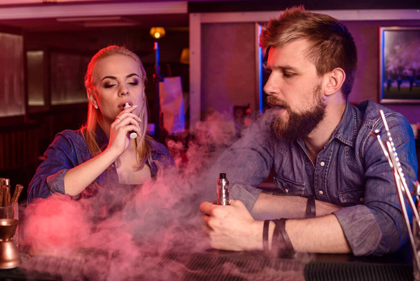 Un homme et une femme fumant une cigarette électronique dans un bar à singes. Magasin de singes - Photo, image