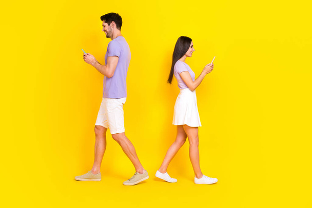 Full size photo of attractive woman man telephone matches walk back to back wear trendy purple look isolated on yellow color background. - 写真・画像
