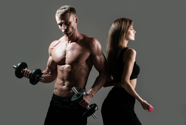 Muscular sexy couple body. Sports people are working out with dumbbells. Fit couple doing exercise with dumbbells in dark studio - Foto, imagen