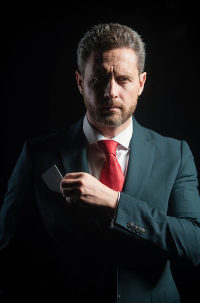 Portrait of an elegant handsome business man isolated on black. Handsome thoughtful middle-aged businessman with credit card in suit posing against a black background with copy space - Foto, imagen