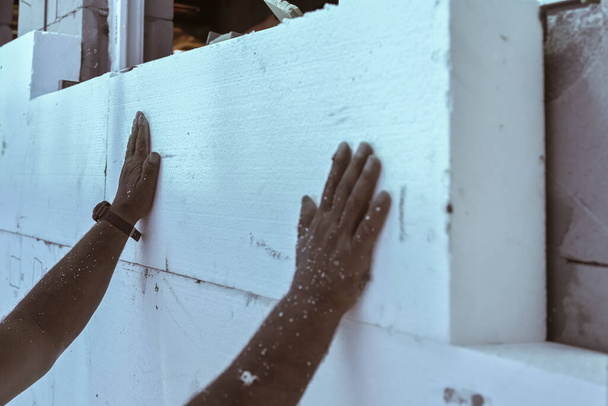 Worker installing polystyrene heat insulation on bare house walls, detail to hand touching white foam boards. - Photo, Image
