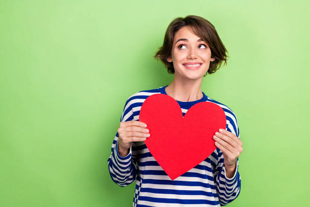 Photo of pleasant cheerful woman bob hairstyle sailor shirt look empty space holding red heart postcard isolated on green color background. - 写真・画像