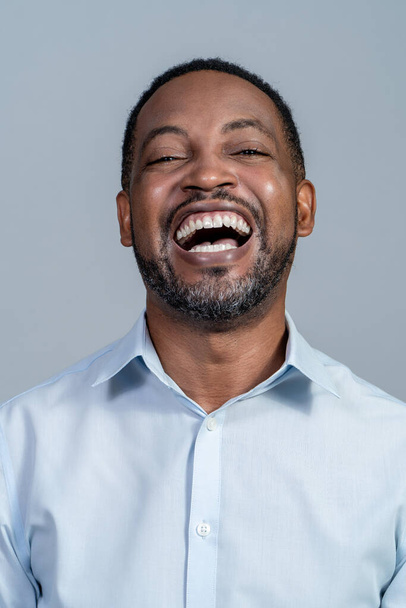 Portrait of a black adult male wearing a light blue dress shirt laughing hysterically - Valokuva, kuva