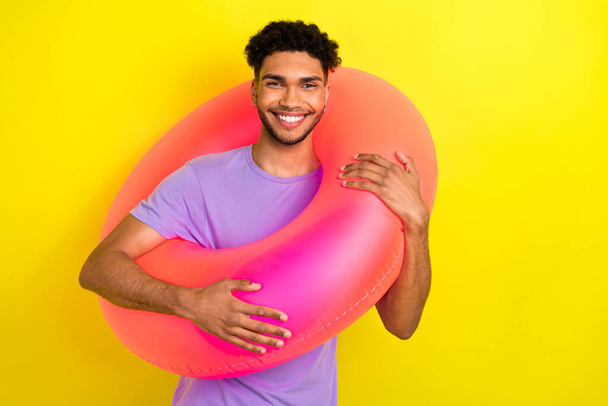 Portrait of positive carefree young man toothy smile hold inflatable ring enjoy summertime isolated on yellow color background. - Фото, изображение