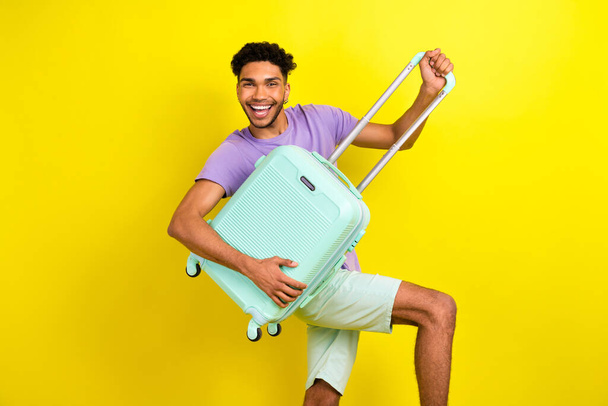 Portrait of overjoyed handsome young person beaming smile arms hold suitcase isolated on yellow color background. - Φωτογραφία, εικόνα