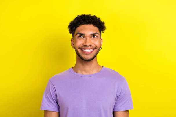 Photo of positive thoughtful guy dressed purple t-shirt looking up empty space isolated yellow color background. - Foto, Bild