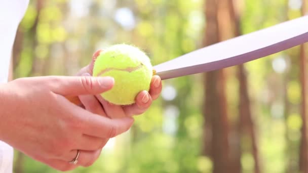 Egy lány letisztítja a teniszlabdát a koszos közeli képekről. Fa ütők és teniszlabda a szabadtéri játékhoz. Szabadtéri tevékenység - Felvétel, videó