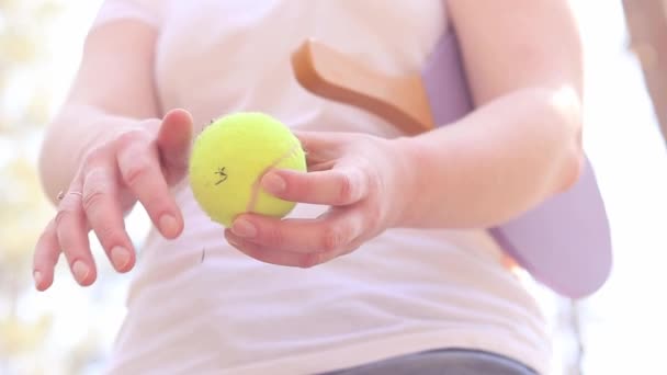 女の子は土の近くからテニスボールをきれいにします。屋外プレイのための木製のラケットとテニスボール。野外活動 - 映像、動画