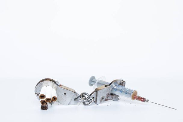 Шприц и сигареты прикованы наручниками на белом фоне, наркомания, плохая привычка - Фото, изображение