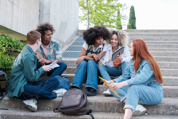 Opiskelijaryhmä jakaa muistiinpanoja istuu ulkona yliopiston kampuksella. Konsepti: opinnot, koulutus, yliopisto - Valokuva, kuva