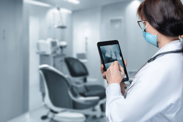 Zahnarzt untersucht einen Zahn auf einem mobilen Tablet in einer Klinik. - Foto, Bild