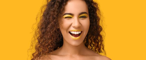 Mujer afroamericana feliz con maquillaje brillante sobre fondo amarillo - Foto, Imagen