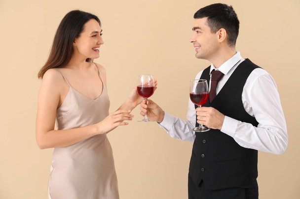 Ο νεαρός δίνει στην κοπέλα του ένα ποτήρι κρασί σε μπεζ φόντο. - Φωτογραφία, εικόνα