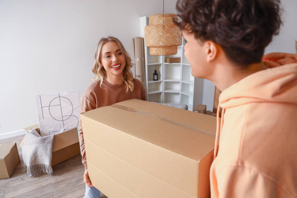 Young couple carrying cardboard box in room on moving day - Photo, Image