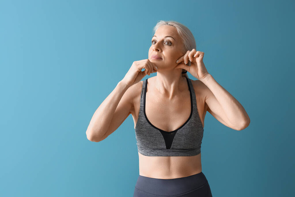 Femme mûre sportive faisant un exercice de renforcement du visage sur fond bleu - Photo, image