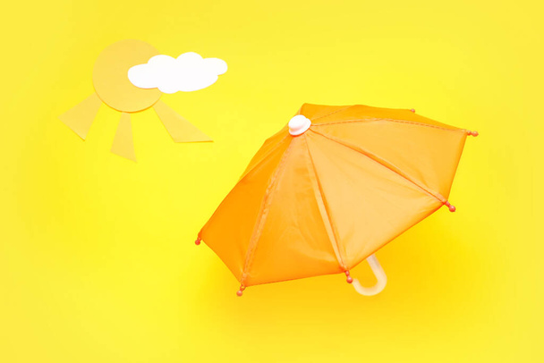 Creative composition with umbrella, paper cloud and sun on yellow background - Photo, Image