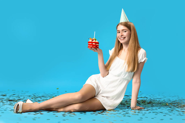 Молодая женщина с праздничным тортом сидит на синем фоне - Фото, изображение