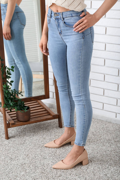 Young woman in stylish jeans and heeled shoes near mirror in room - Foto, Imagem
