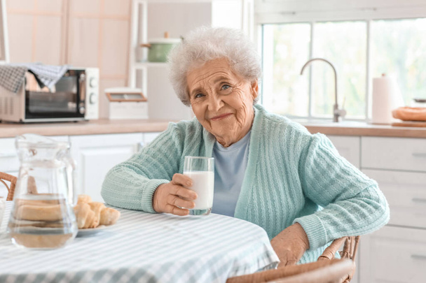 Senior woman with glass of milk in kitchen - Foto, afbeelding