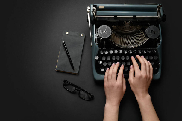 Žena psaní na psacím stroji s brýlemi, notebook a pero na černém pozadí - Fotografie, Obrázek