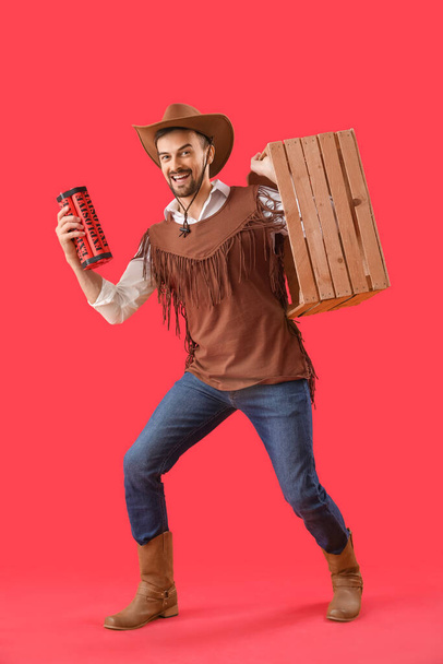 Handsome cowboy with explosive and wooden box on red background - Photo, Image