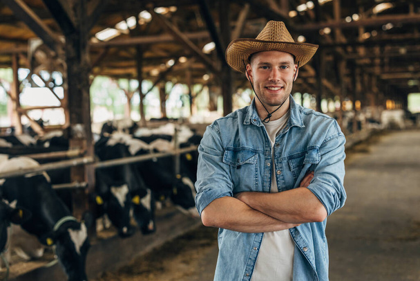 Portrait of a happy farmer standing in a barn full of cows. - 写真・画像