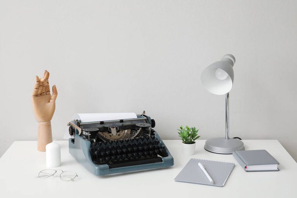 Vintage machine à écrire avec lampe, main en bois et cahier sur table blanche près du mur - Photo, image