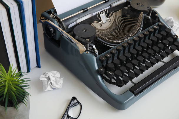 Máquina de escrever vintage com livros, plantas de sala e óculos na mesa perto da parede bege - Foto, Imagem