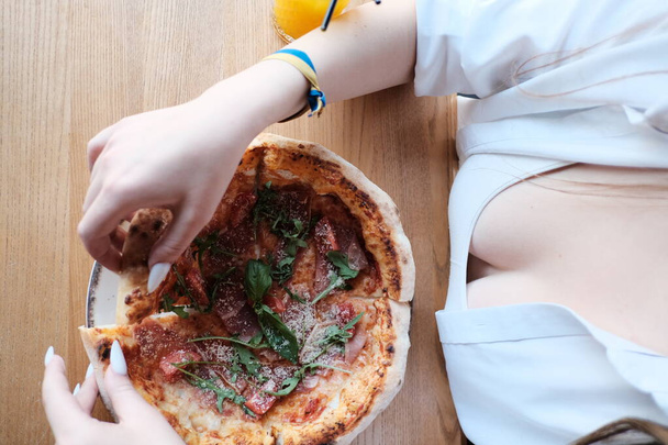 Ústní pohled na lahodnou pizzu Prosciutto s rajčaty, sýrem a rukolou, elegantně prezentovanou na venkovském dřevěném stole. - Fotografie, Obrázek